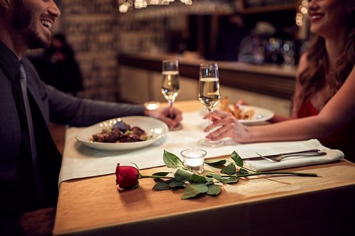 Twee personen aan tafel tijdens een romantisch diner met glzen bubbels en een roos op tafel